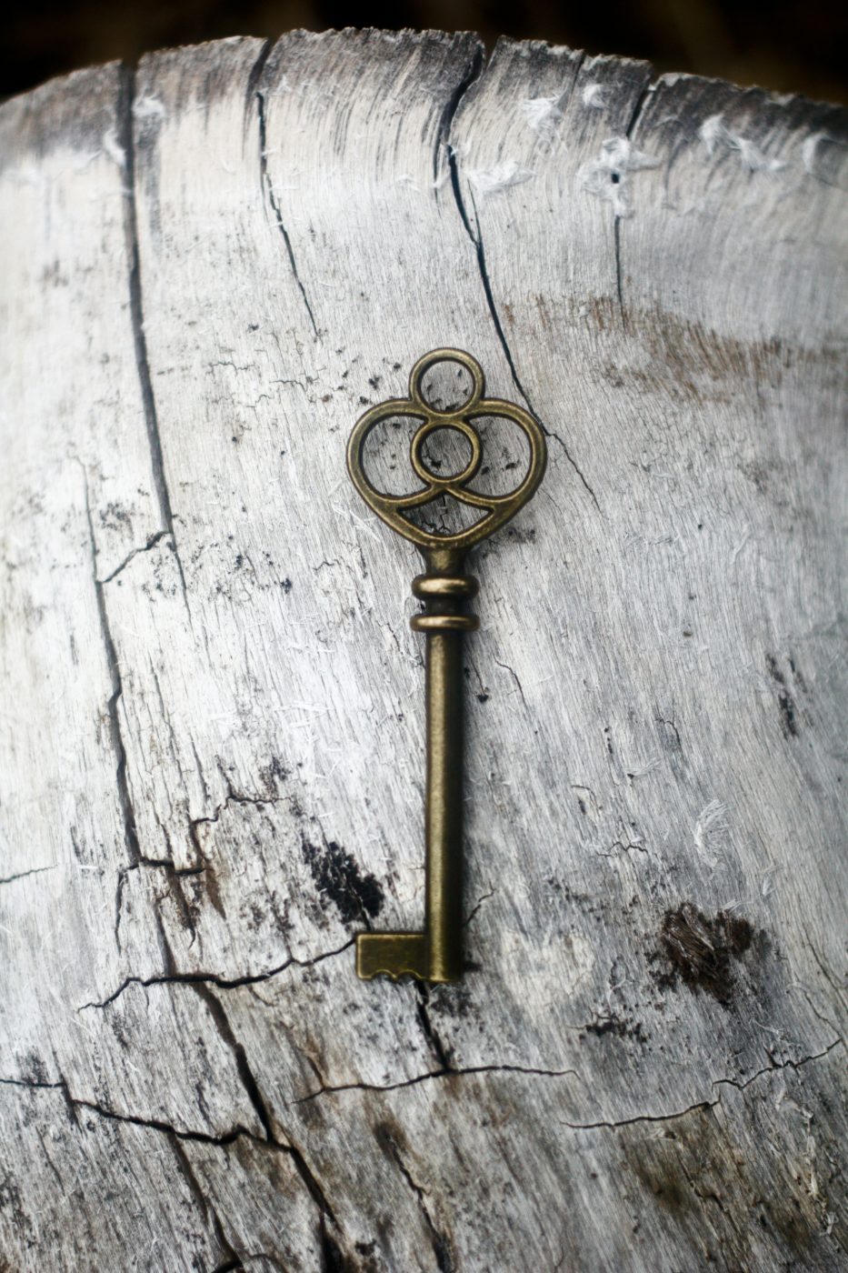 An ornate brass key resting on weathered, pale wood with fine cracks and grain.
